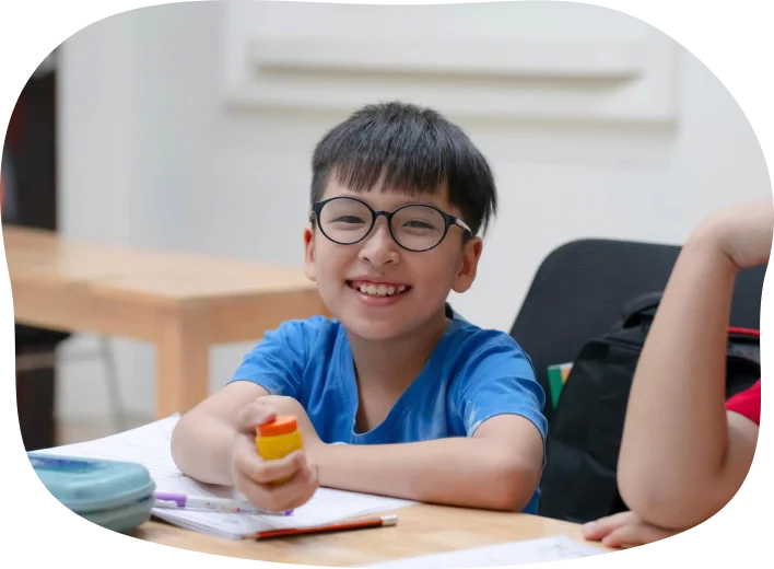 Học sinh tươi cười cầm bút tại bàn học